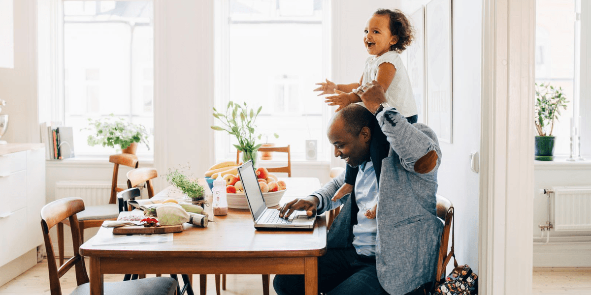 Vader werkt lachend aan tafel, heeft zijn lachende dochter op zijn schouders
