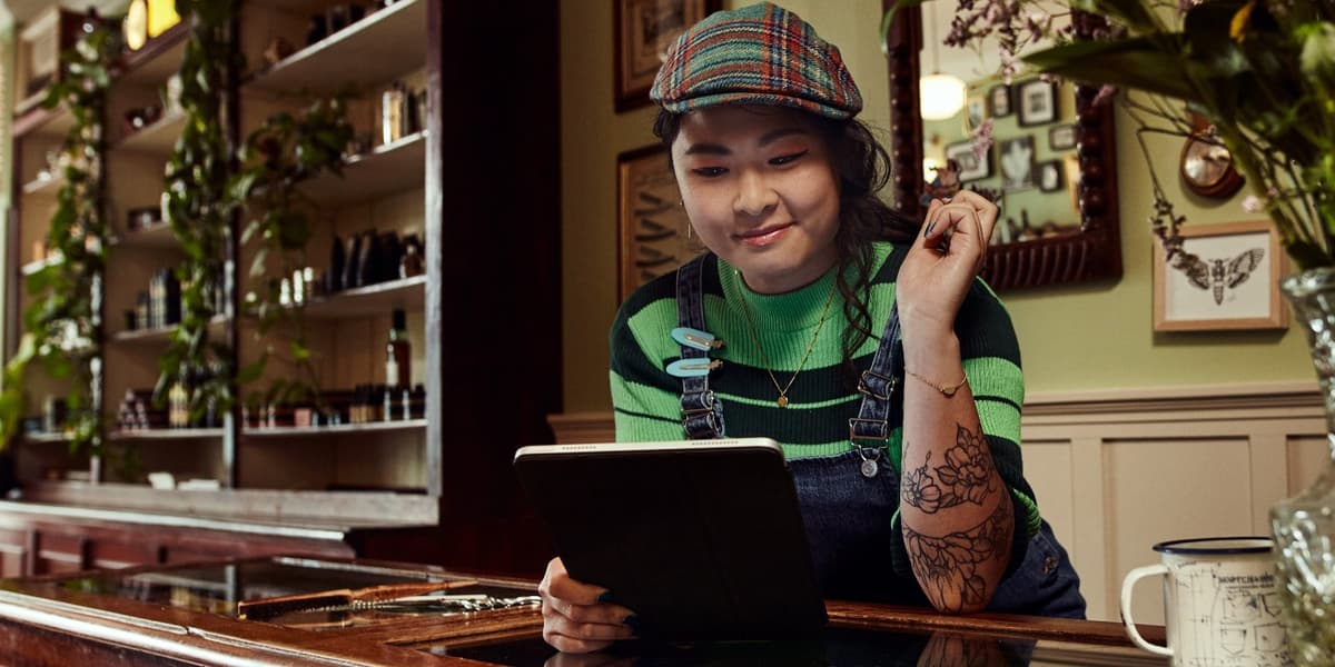 Kapster staat aan haar balie, heeft een tablet in haar hand