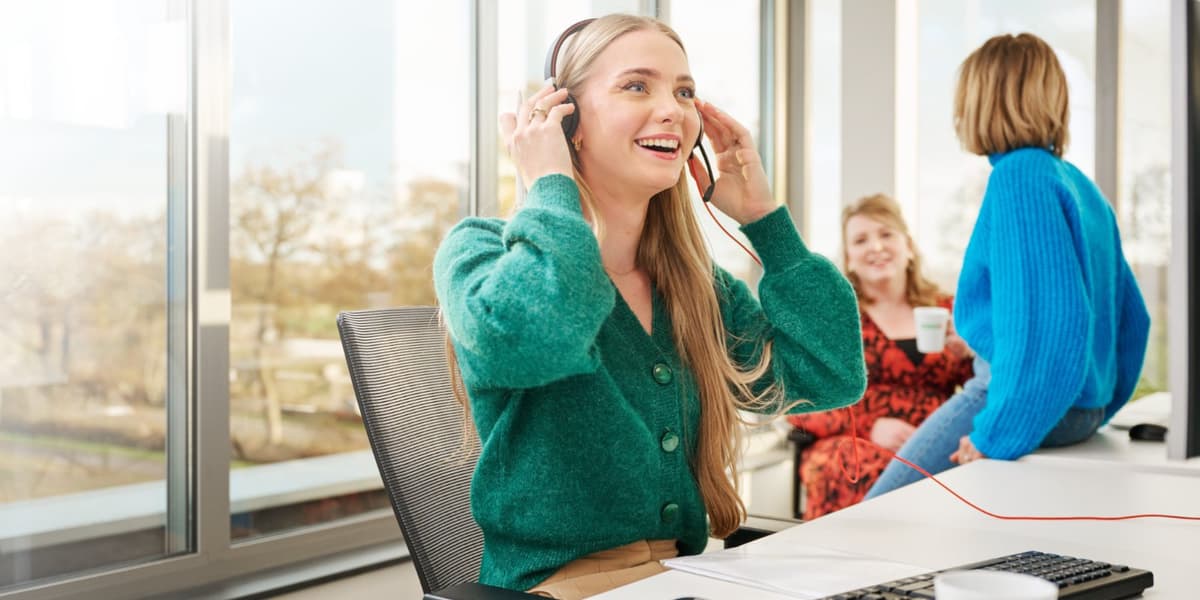 Jurist lachend aan de telefoon met haar headset op, twee collega's in gesprek op de achtergrond