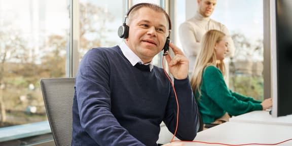 Jurist aan de telefoon met headset op, twee collega's overleggen op de achtergrond