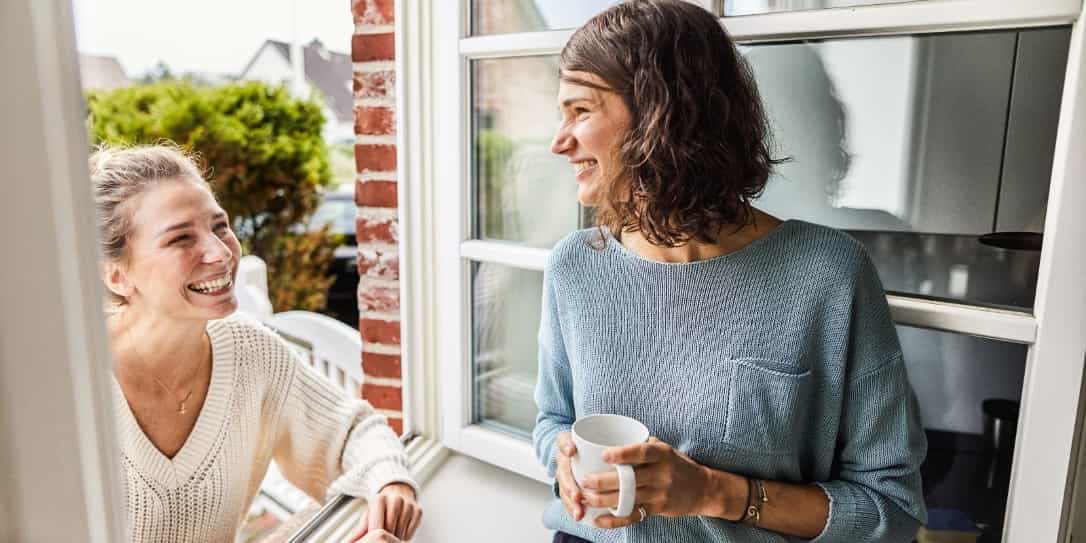 Vrouw heeft in haar raamopening een leuk gesprek met haar buurvrouw