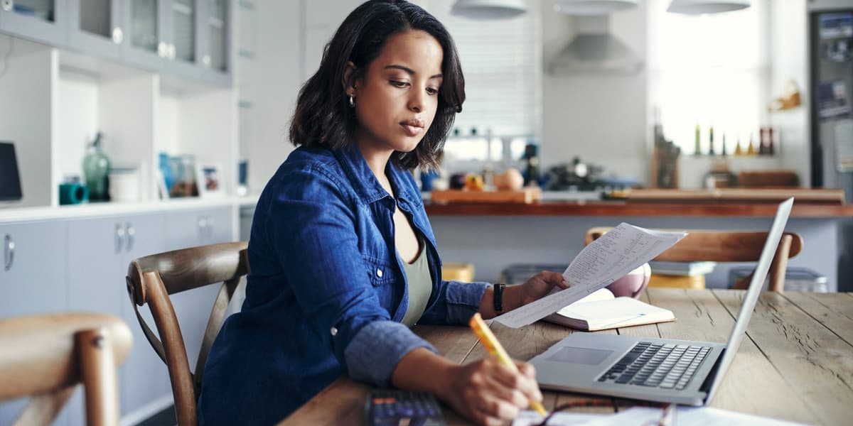 Vrouw werkt aan haar keukentafel, heeft pen en papier in de hand en schrijft iets op