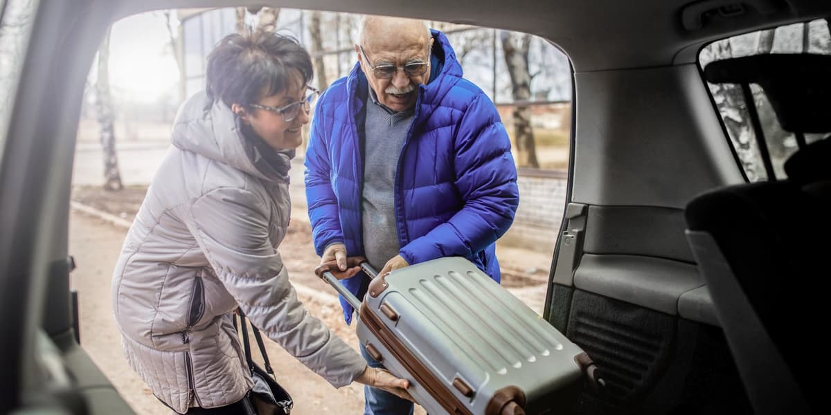 Een man en vrouw leggen samen hun reiskoffer achterin de auto