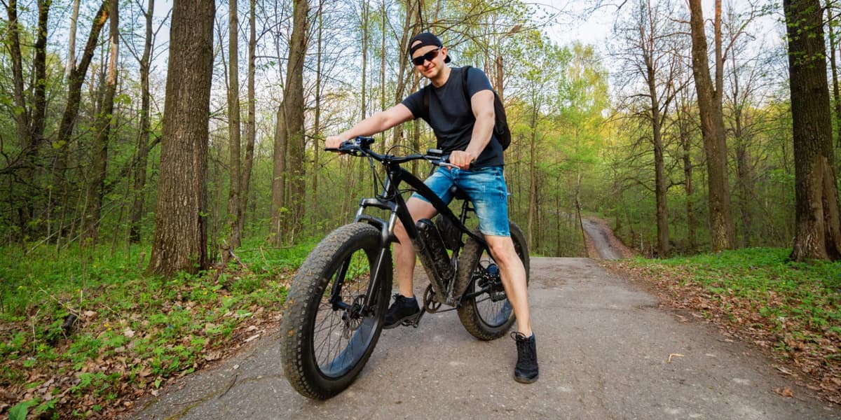 Man met pet en zonnebril staat in het bos stil met zijn fatbike