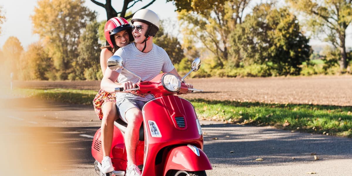 Een stel rijdt lachend op een rode scooter