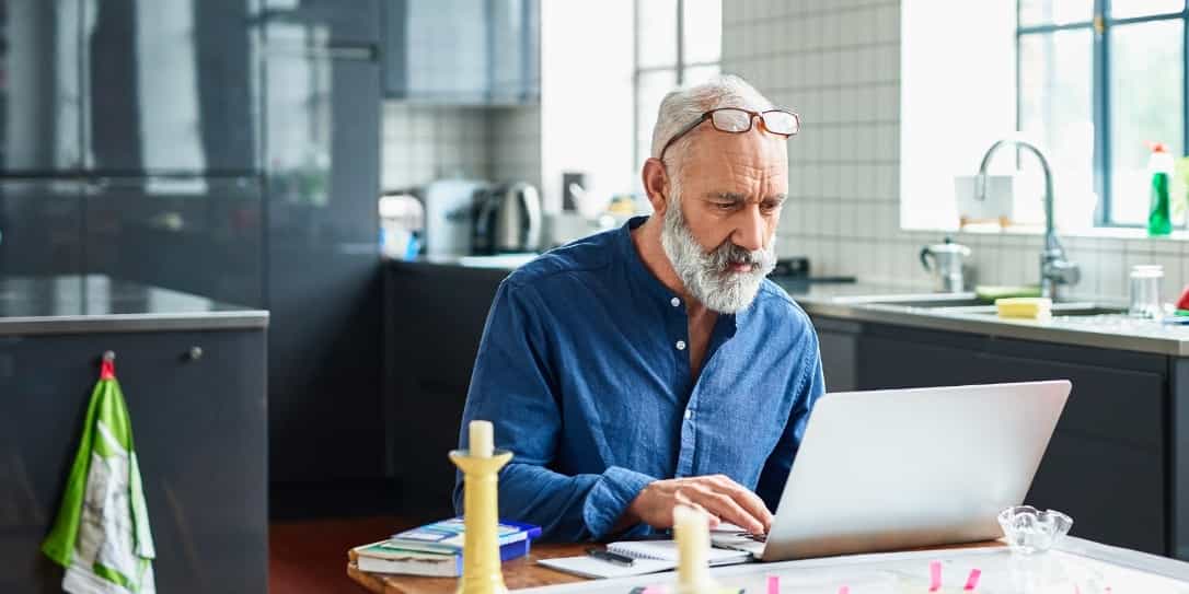Man in zijn keuken kijkt bedenkelijk naar zijn laptop